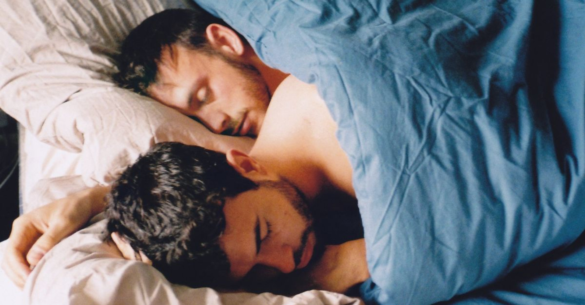 Two men in bed looking at each other lovingly