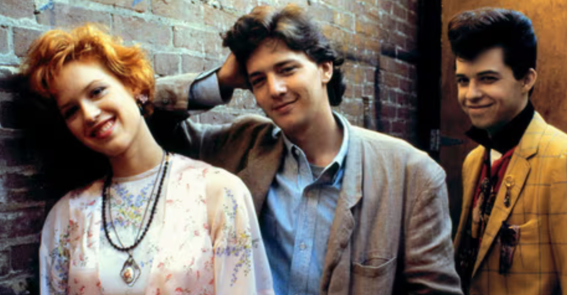 Three young adults by a wall smiling